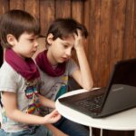 Genitore in smart working con laptop e bambino che gioca, simbolo delle nuove regole per famiglie.